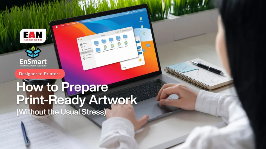 Designer preparing artwork for printing on a laptop for EAN Label printing and packaging supplier and manufacture Malaysia, showing workspace with notes and tools