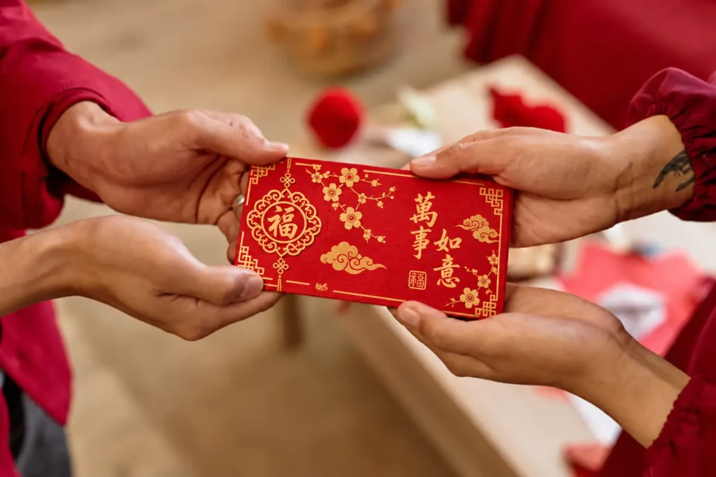 Hands exchanging a custom red angpao packet decorated with gold Chinese New Year patterns