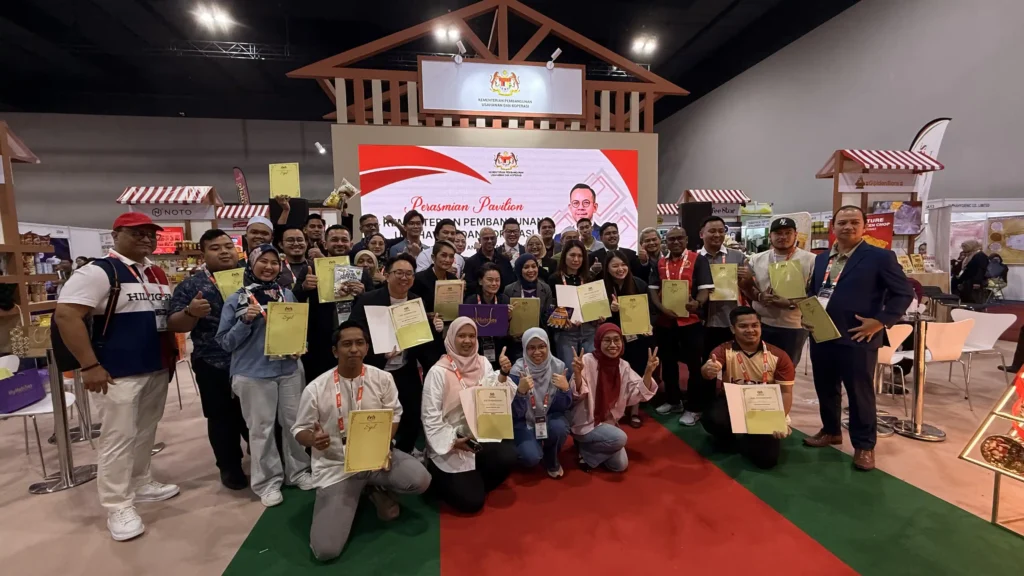 Entrepreneurs and exhibitors holding certificates and packaged products at a MIHAS 2026 pavilion event